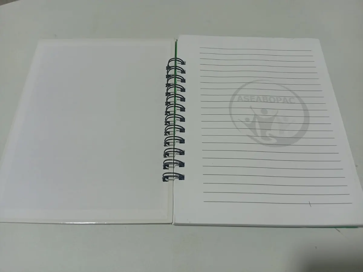 Cuaderno de tapa dura abierto con anillado metálico wire-o negro y primera hoja con marca de agua