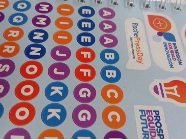 Hoja de stickers con letras y logos dentro de un cuaderno con espiral