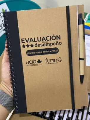 Libreta kraft con lomo negro, bolígrafo y portada con título y logotipos